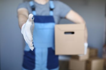 Worker extends white-gloved hand towards viewer while holding brown package in other hand