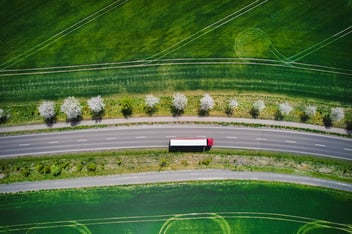  A heavy goods vehicle seen from above on a clear road passing through green fields represents the swift service you might get with a transportation optimization platform.