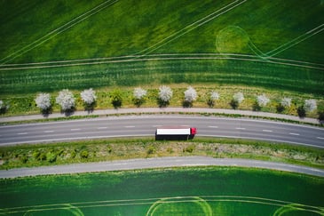  A heavy goods vehicle seen from above on a clear road passing through green fields represents the swift service you might get with a transportation optimization platform.